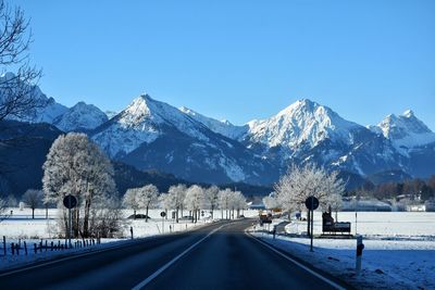 Road by snowcapped mountains against clear blue sky