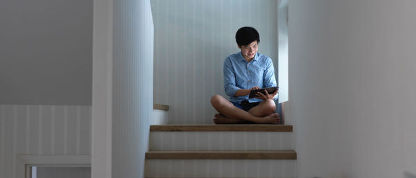 Low angel view of young man holding digital tablet sitting on staircase