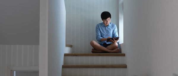 Low angel view of young man holding digital tablet sitting on staircase
