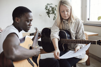 Young male student reading musical note with female tutor in classroom