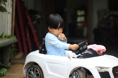 Cute girl eating food while sitting in toy car