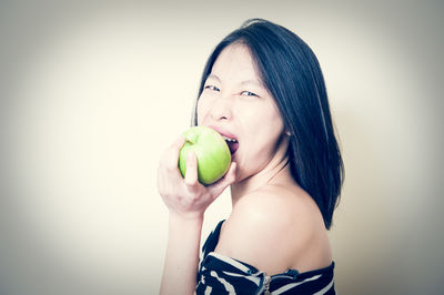 Portrait of young woman holding apple against white background