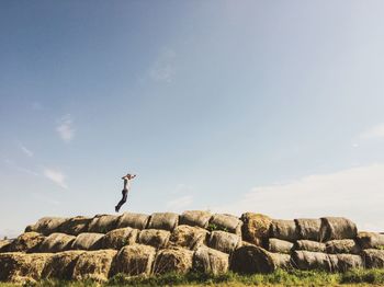 Man jumping on hay bales against sky