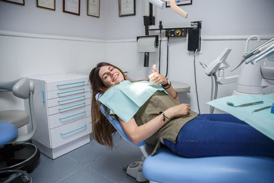 Portrait of smiling young woman showing thumbs up on dentist chair