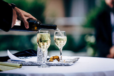 Cropped hand of person pouring drink in glass on table