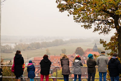 Rear view of people in warm clothes standing by railing in town