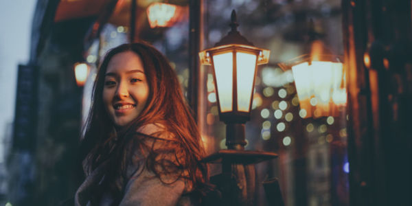 Portrait of smiling young woman standing against illuminated lights