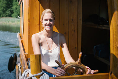 Portrait of smiling woman sitting by wheel in boat on lake