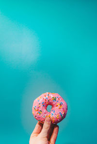 Cropped hand holding donut against blue background