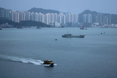 Boat sailing on sea by city against sky