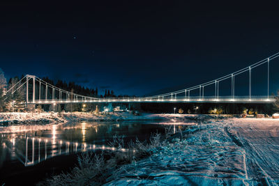 Illuminated bridge over river against sky at night