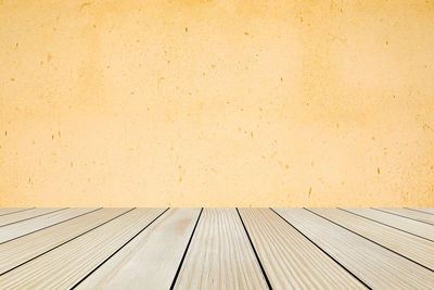 Close-up of wooden floor against yellow wall