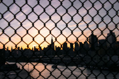 Silhouette fence by buildings against sky during sunset