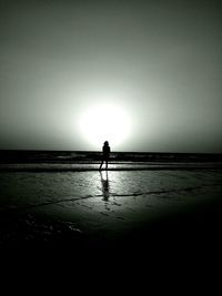 Silhouette man walking on beach against clear sky