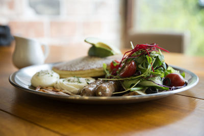 Close-up of pancakes with salad and sausage served in plate on wooden table