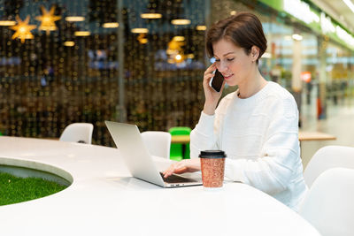 Woman talking on smart phone using laptop at table