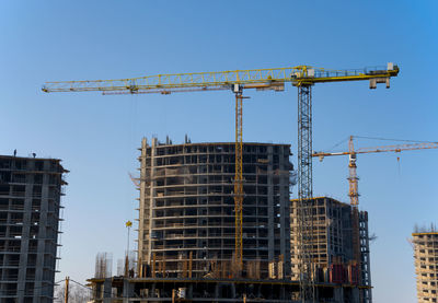 Low angle view of crane by building against sky