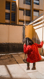 Rear view of woman with red umbrella against building