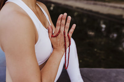 Midsection of woman with hands clasped holding prayer beads
