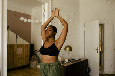 Young woman exercising with eyes closed and arms raised at home