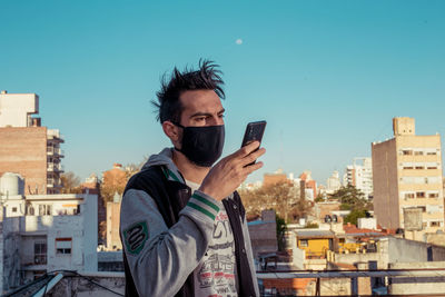 Portrait of young man photographing cityscape against sky