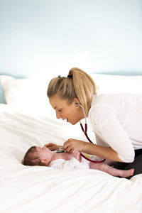 Side view of female pediatrician examining baby girl lying on bed