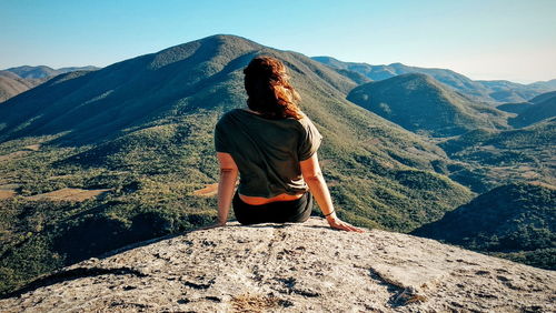 Rear view of woman sitting on mountain against sky