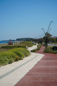 Empty road by sea against clear blue sky