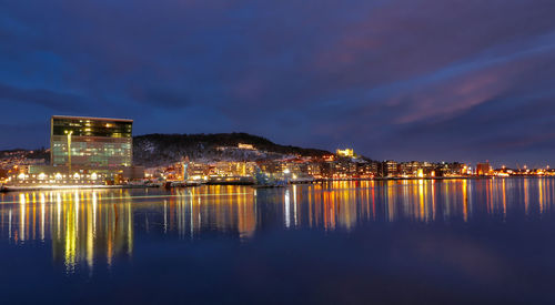 Illuminated city by sea against sky at night