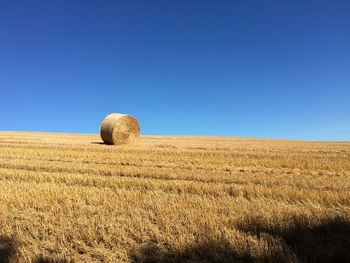 Hay bales on field against clear blue sky