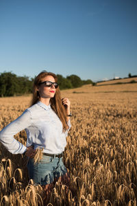 Portrait of young woman standing in field against clear blue sky