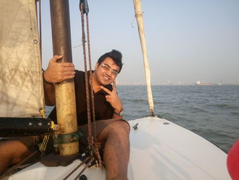 Portrait of young man gesturing peace sign while sitting in sailboat over sea