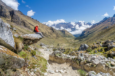 Side view of hiker relaxing on rock at mountain against blue sky