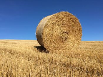 Hay bales on field against clear blue sky