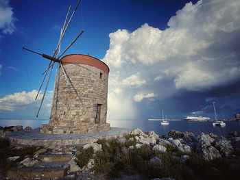 Traditional windmill by sea against sky