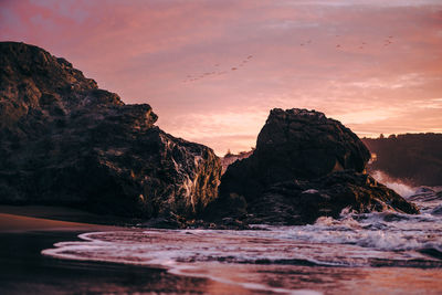 Rocks by sea against sky during sunset