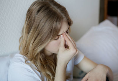 Young woman suffering from headache sitting on bed at home