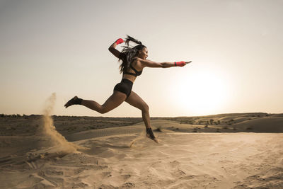 Woman jumping on desert against clear sky