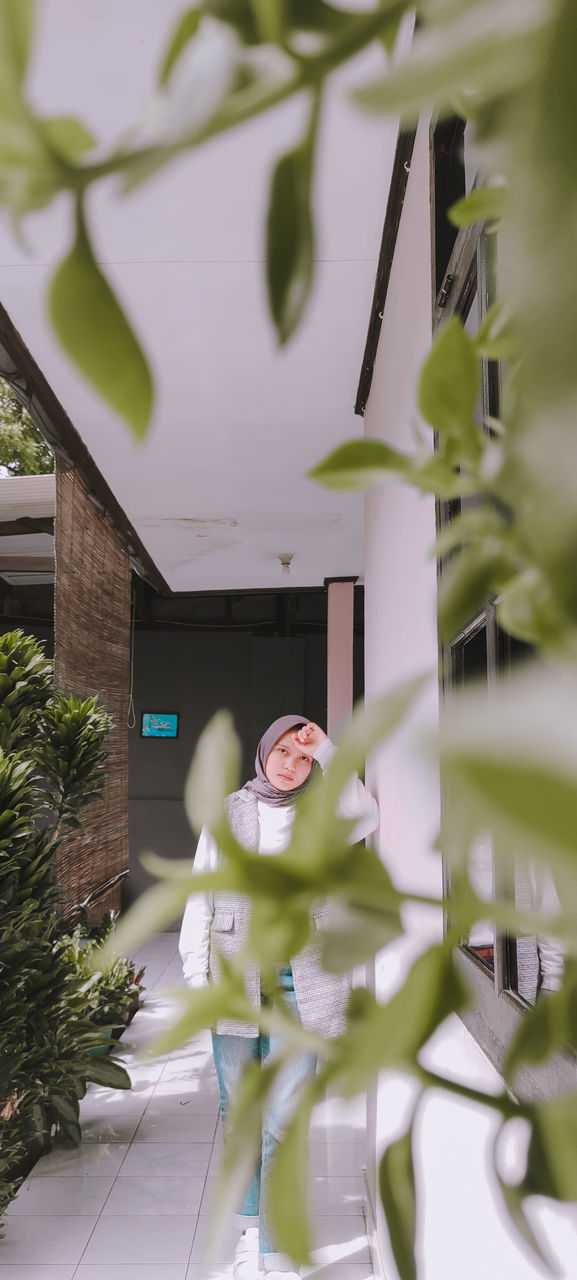 WOMAN STANDING BY TREE AGAINST HOUSE