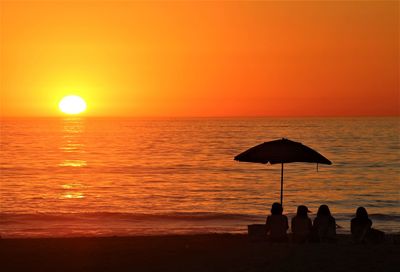 Silhouette people relaxing at beach during sunset