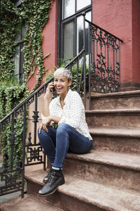 Portrait of happy woman talking on mobile phone while sitting on steps