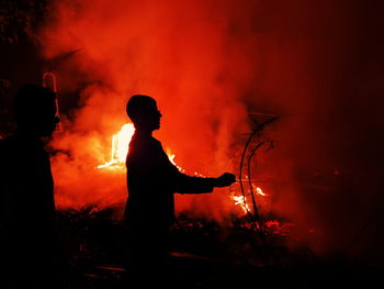 Silhouette man against orange fire at night