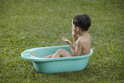 Shirtless boy sitting in bathtub on field at yard