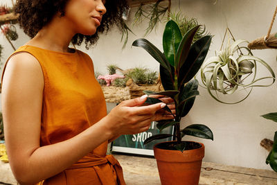 Midsection of woman using mobile phone at potted plant