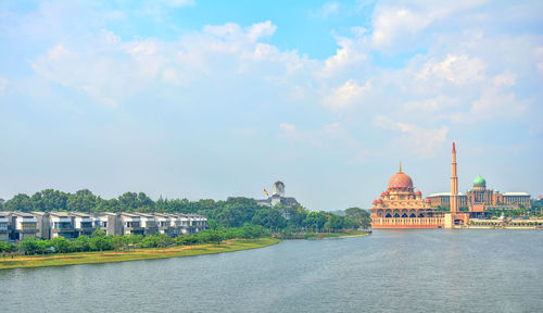 View of buildings by river against cloudy sky