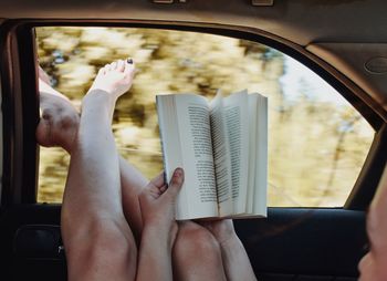 Low section of woman reading book while traveling in car