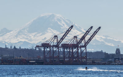 Cranes by sea against sky