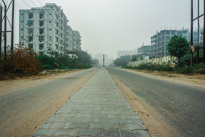 Road by buildings in city against clear sky