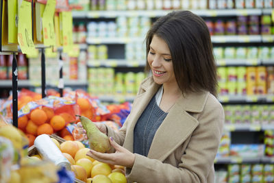 Smiling young woman holding pear in store