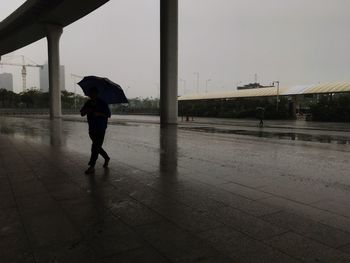 Rear view of man walking on wet glass during rainy season